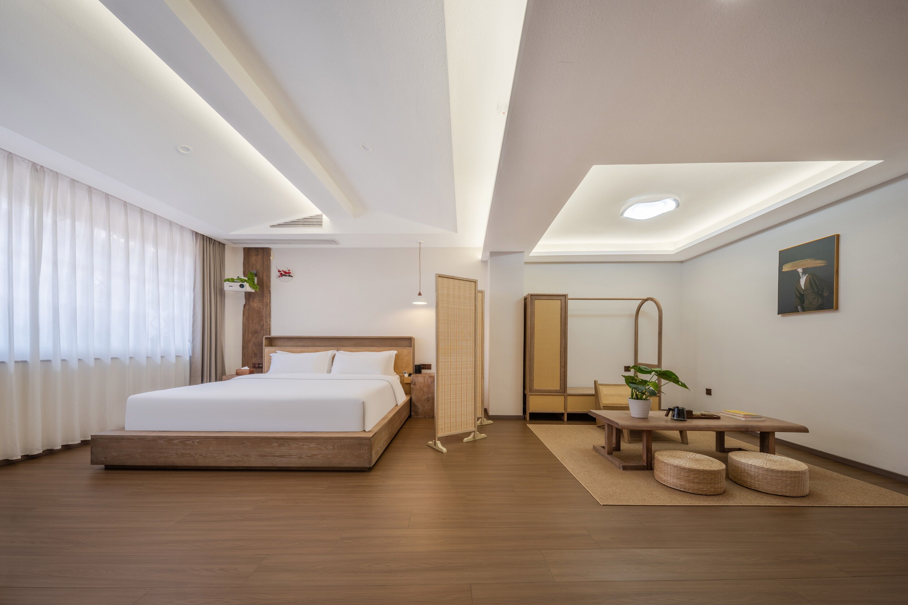 Una habitación de hotel moderna con una cama grande, mesitas de noche y una pequeña zona de estar con otomanas.
