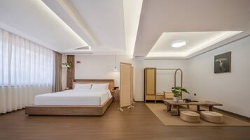 Una habitación de hotel moderna con una cama grande, mesitas de noche y una pequeña zona de estar con otomanas.