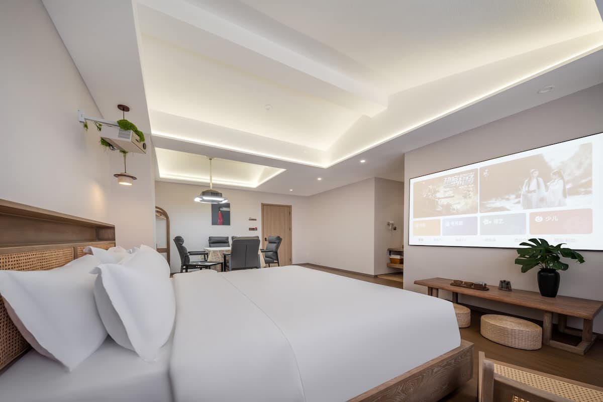 A modern hotel room with a large bed, a desk, and a projector screen displaying images.
