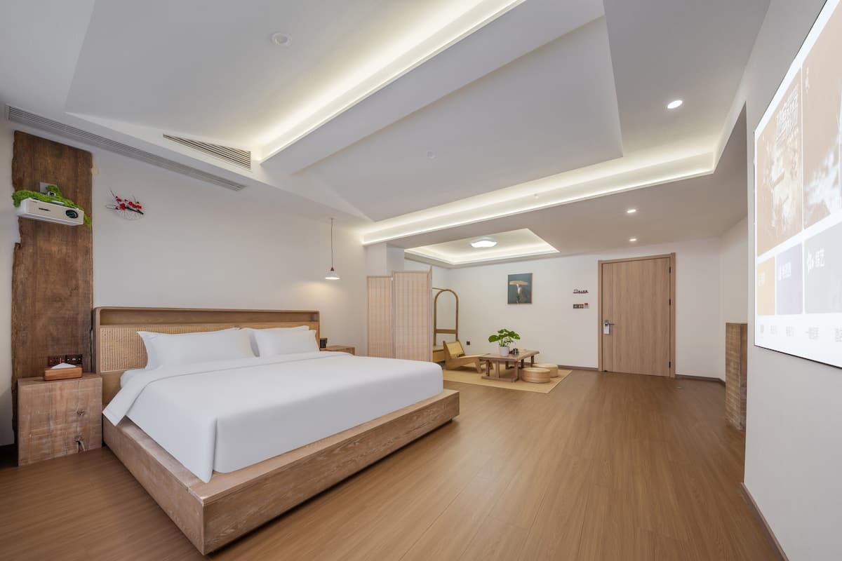 A modern hotel room with a large bed, wooden flooring, a desk, and a seating area.