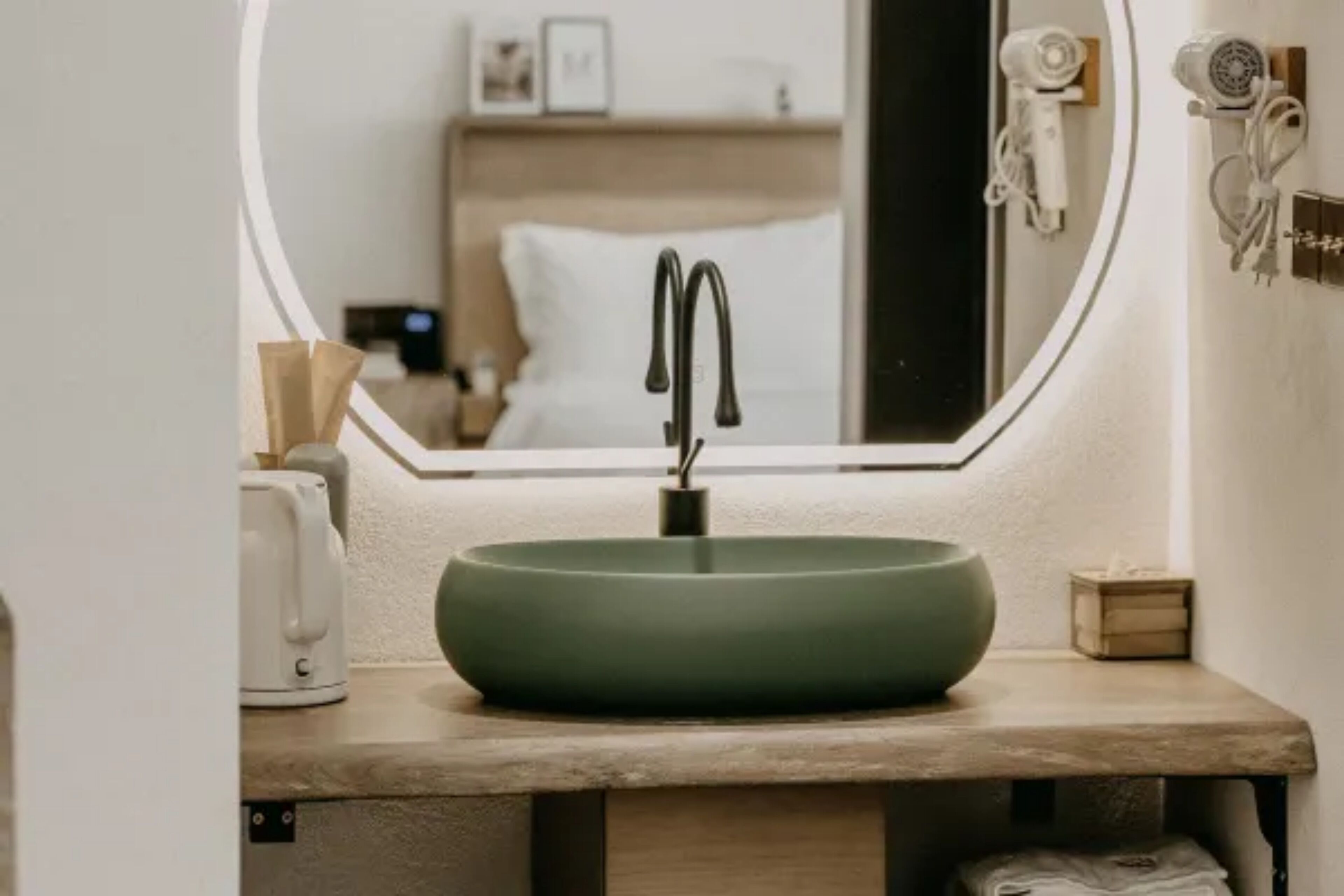 A bathroom with a round green sink, a mirror, a hairdryer, and a towel rack.