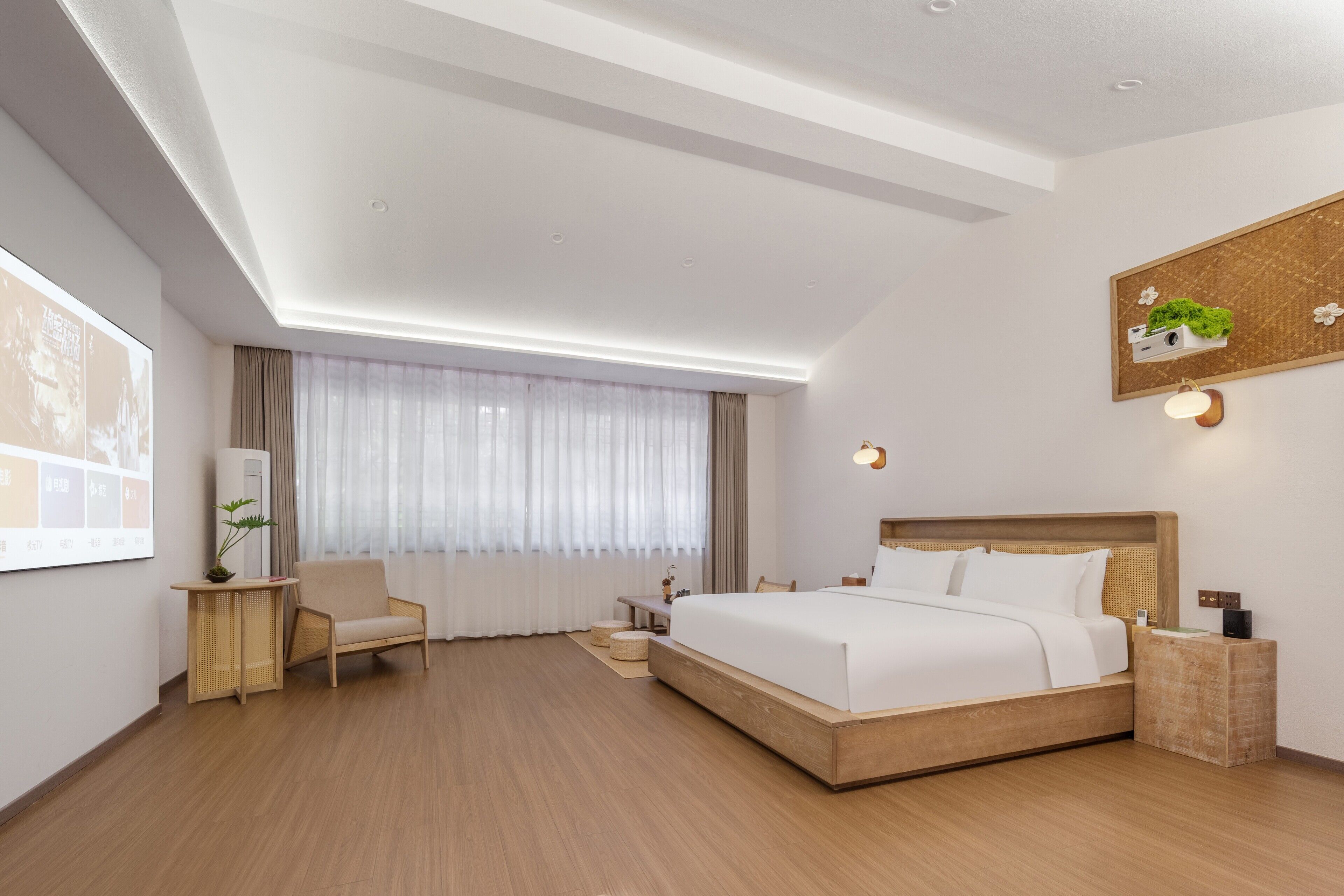 A modern hotel room with a large bed, a wooden floor, a desk with a chair, a small table, and a large window with curtains.