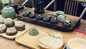 Um conjunto de chá tradicional sobre uma bandeja de madeira, com uma cesta trançada, uma chaleira verde e vários bules e xícaras.