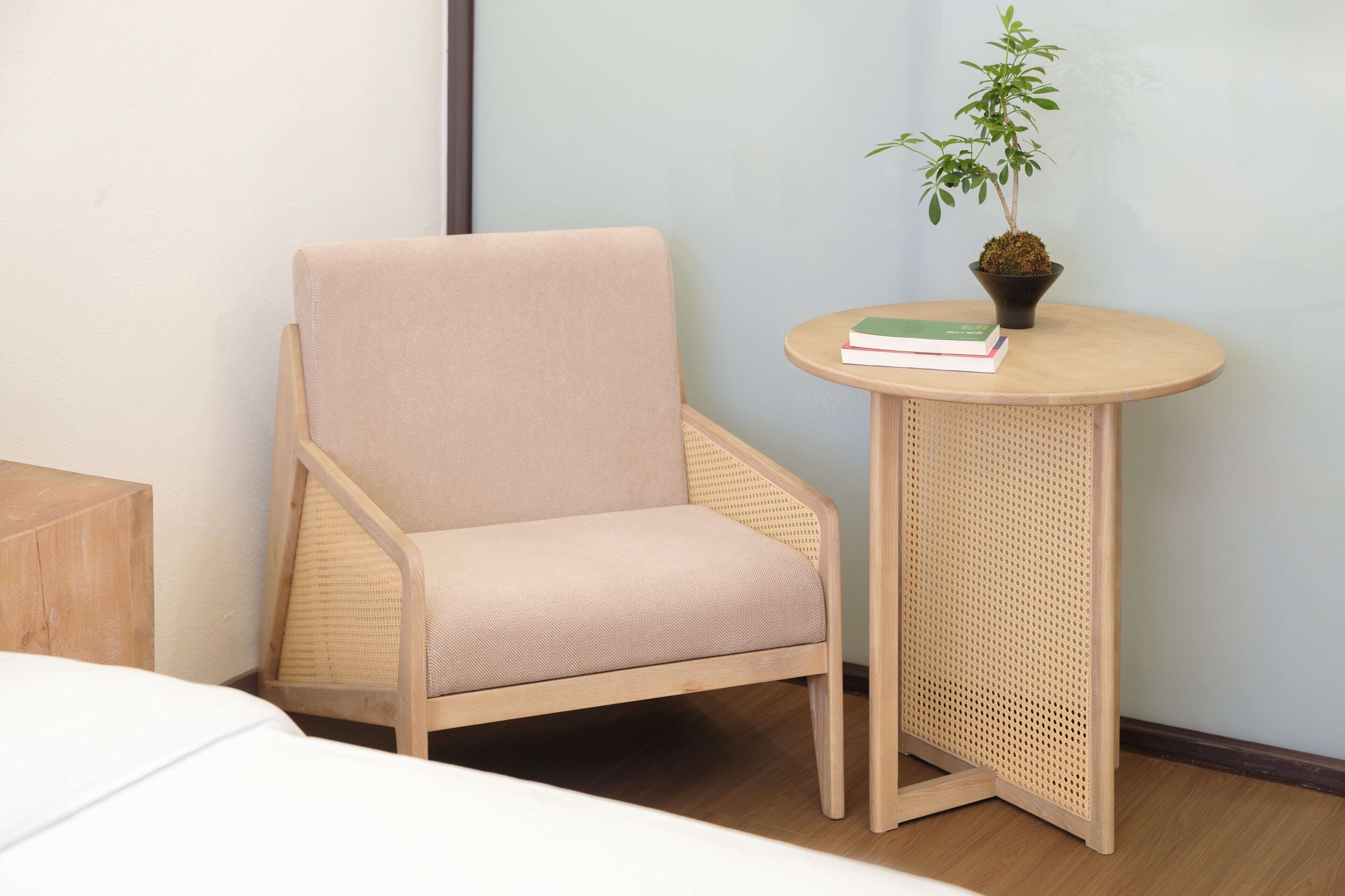 Une pièce comprenant un fauteuil recouvert d’un tissu beige, une petite table ronde ornée d’une plante en pot et d’un livre, ainsi qu’une table de chevet en bois.