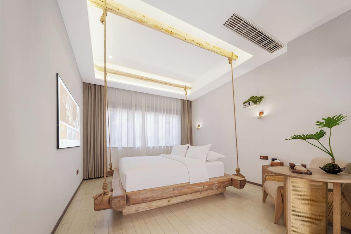 A modern hotel room with a wooden swing bed, a wooden table, and a potted plant.