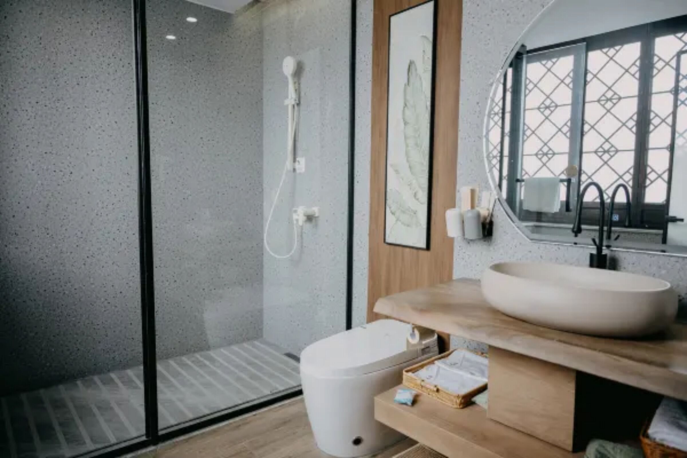 A modern bathroom with a glass shower enclosure, a wooden vanity with a large sink, and a framed artwork on the wall.