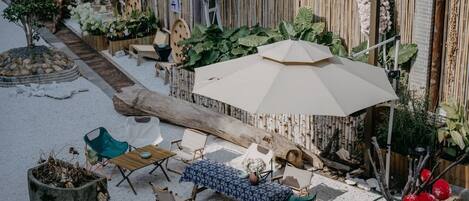 Un área de estar al aire libre con una mesa, sillas, un paraguas grande y una estructura de madera.