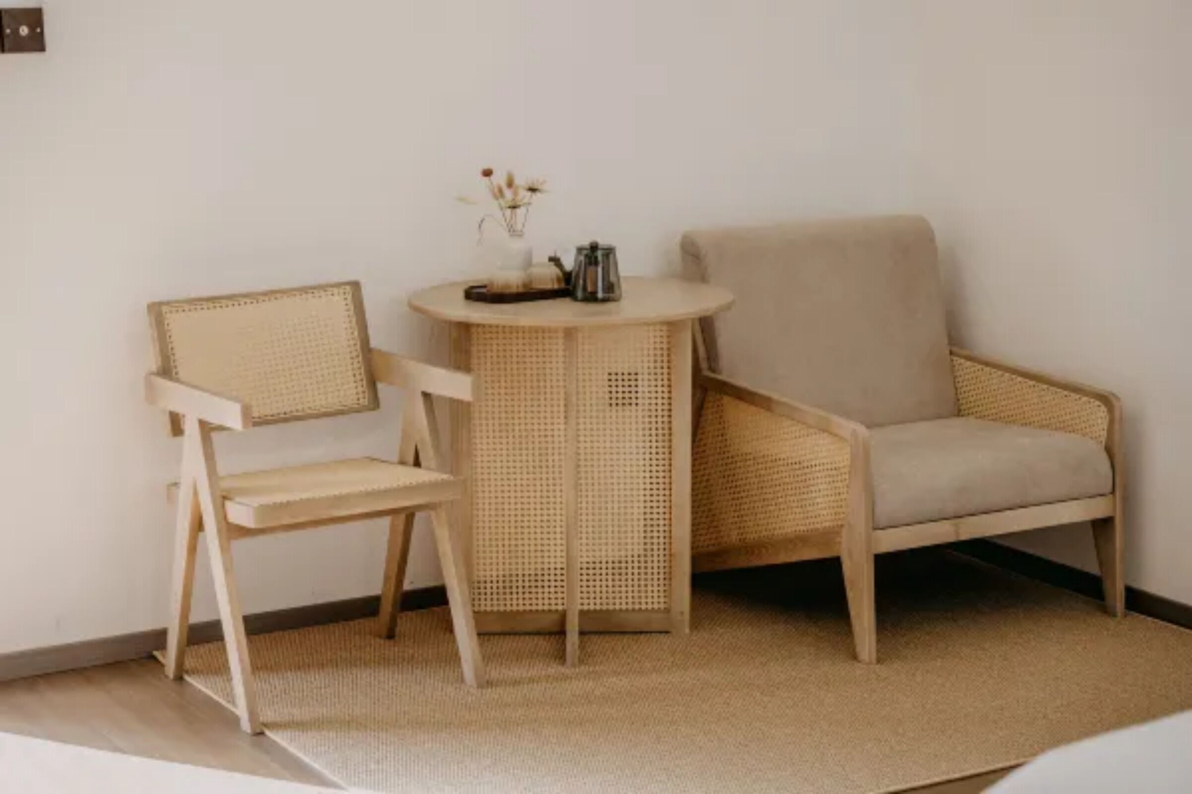A room with a round table, two wicker chairs, and a beige armchair.