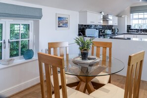 A modern kitchen with white cabinets, a glass dining table, and wooden chairs. - Caldey View Cottage - 1 Bedroom - Penally (Tenby)
