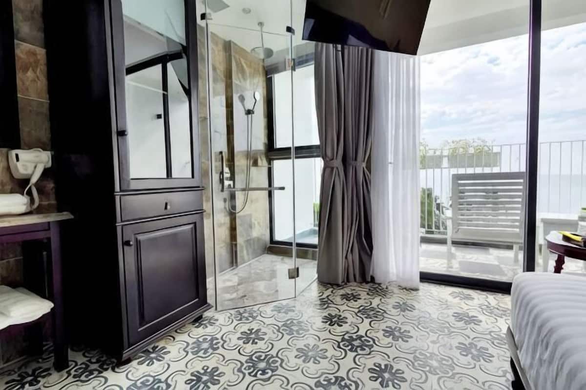 Ein modernes Hotelzimmer mit Duschkabine aus Glas, einem Balkon mit Blick und einem gemusterten Boden.