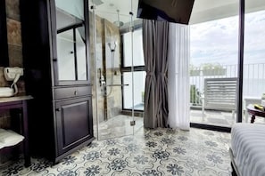 Habitación de hotel moderna con cabina de ducha de vidrio, balcón con vistas y suelo estampado.