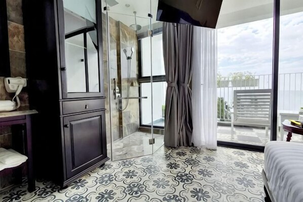 Quarto de hotel moderno com box de chuveiro de vidro, varanda e vista, além de piso estampado.