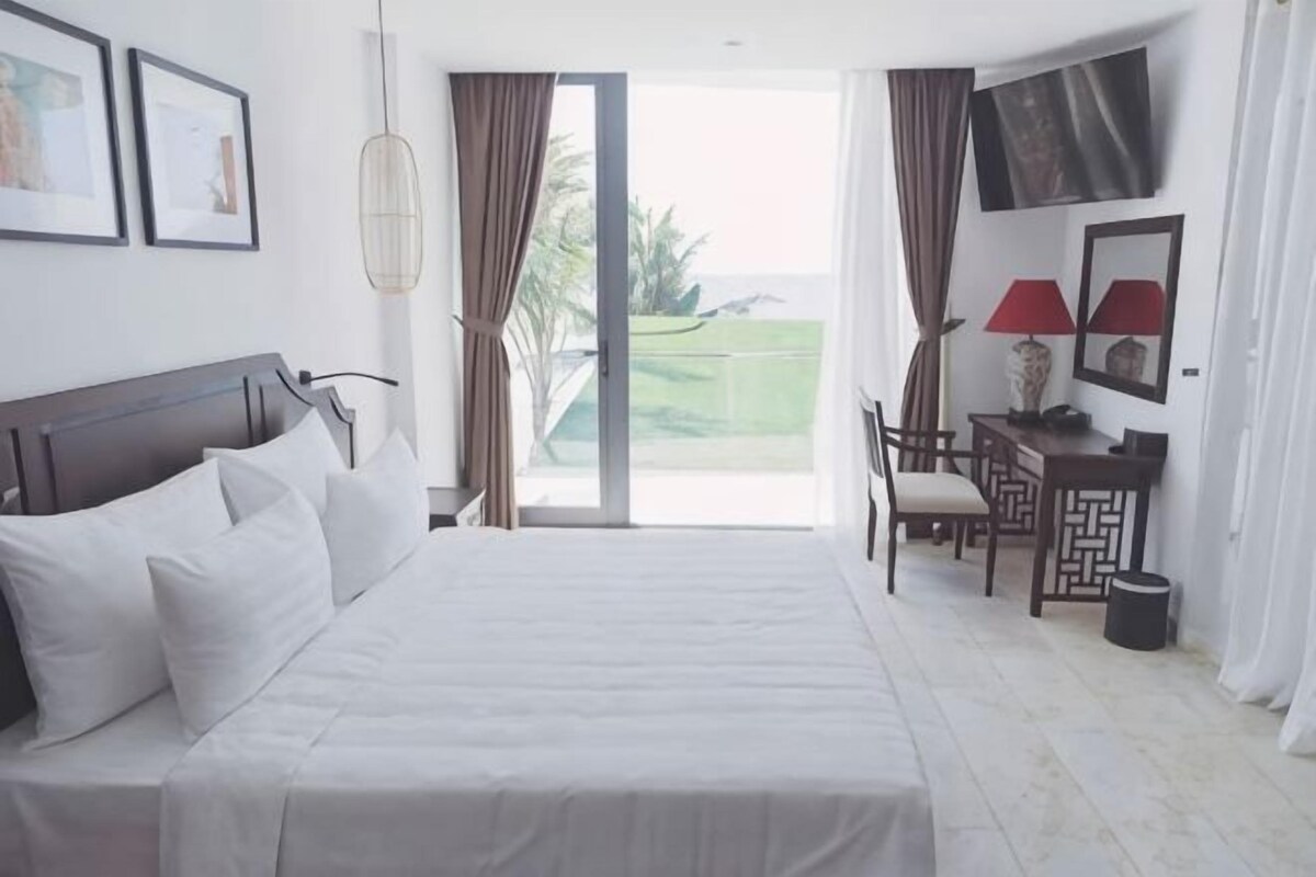 Habitación de hotel con cama, escritorio, silla, televisor y vistas al exterior.