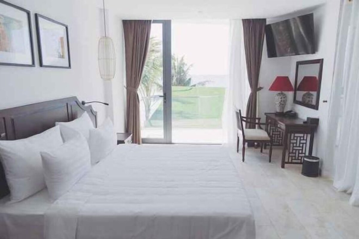A hotel room with a bed, a desk, a chair, a TV, and a view through a glass door.