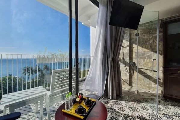 A balcony with a view of the ocean, a white chair, a tray with a beverage, and a glass door leading to a shower area. - The Palmy Phu Quoc Resort & Spa (Phu Quoc Island)