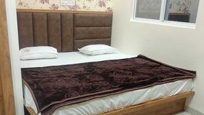 A single bed with a wooden frame, a dark brown blanket, and a headboard with a floral wallpaper pattern. - OM TRINETRA PALACE (Ujjain)