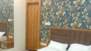 A bedroom with a wooden bed frame, white bedding, and a dark patterned throw. - OM TRINETRA PALACE (Ujjain)