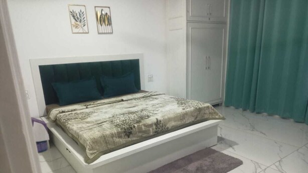 A bedroom with a bed, a headboard, a wardrobe, and a curtain. - OM TRINETRA PALACE (Ujjain)