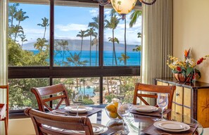 Un coin repas avec une table dressée pour deux personnes, une vue sur l’océan et un paysage tropical.