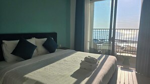 A hotel room with a large bed, a view of the beach, and a balcony with a railing. - Marina Hillside Condotel (An Thoi)
