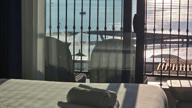 A hotel room with a bed, a view of the beach, and a balcony with chairs and a table. - Marina Hillside Condotel (An Thoi)