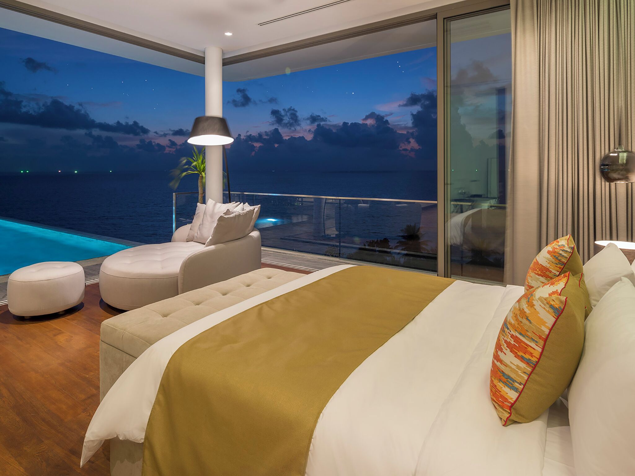 A bedroom with a large bed, a view of the sea, and a pool.