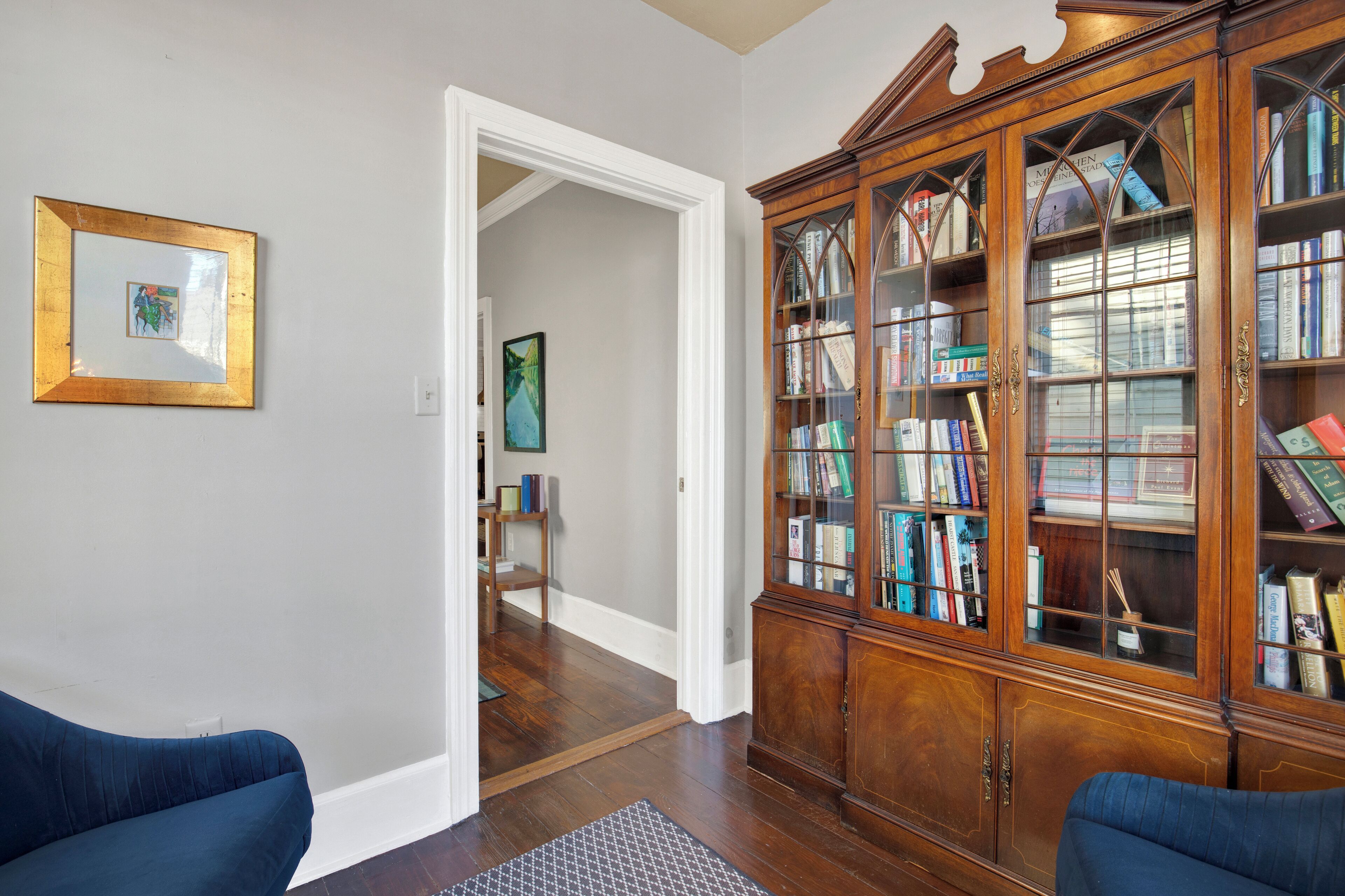 A room with a wooden bookcase, a framed picture on the wall, and two blue sofas.
