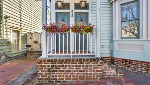 A house with a brick porch, white railings, and flower baskets. - Creative Comfort in Downtown Savannah | Heated Pool Access (Savannah)
