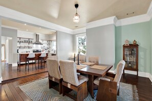 Un comedor amplio con una mesa y sillas de madera, una cocina al fondo y un ventanal que proporciona luz natural.
