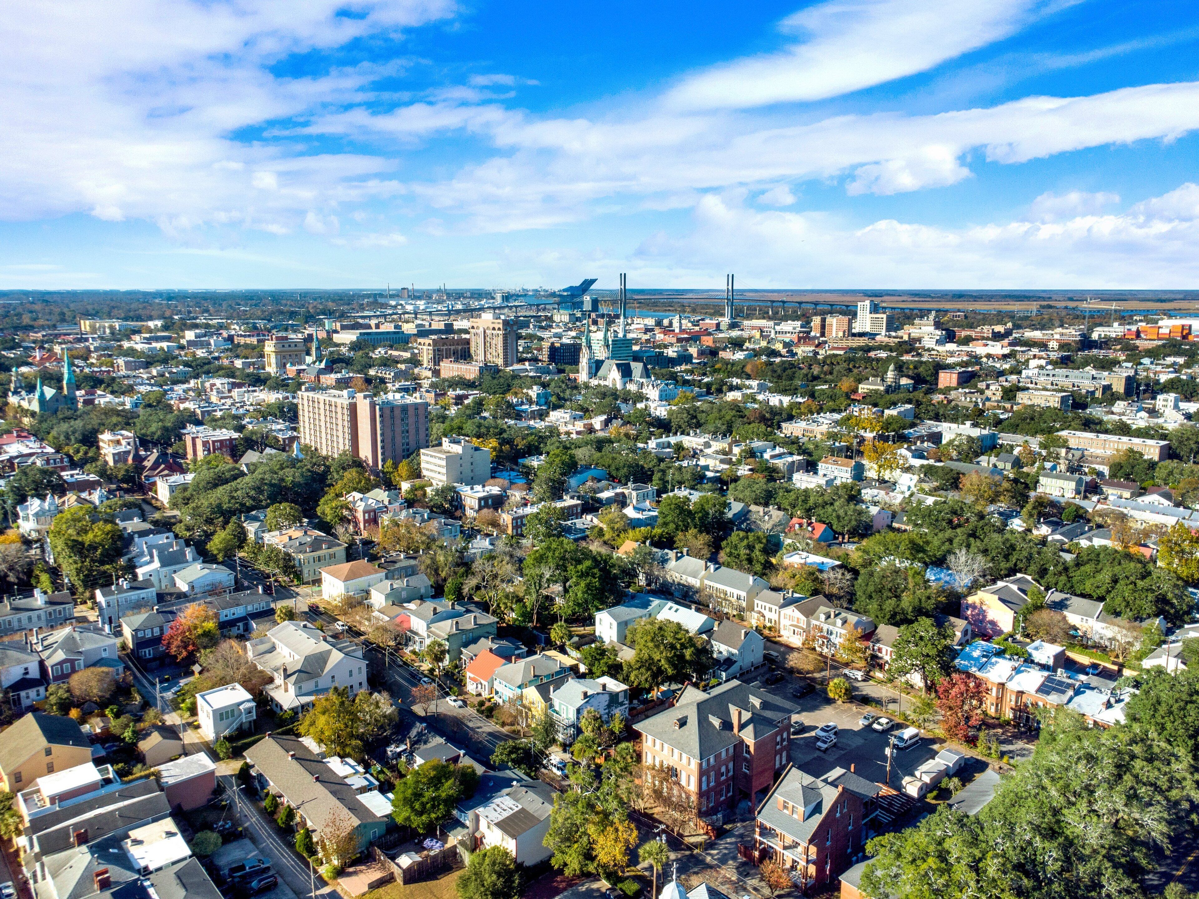 An aerial view of a densely populated urban area with a mix of residential and commercial buildings, a prominent bridge, and a large industrial facility in the distance.