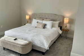 A bedroom with a large bed, two bedside tables, a nightstand, and a matching ottoman. - Loop, New Luxurious Large 3BR, Sleeps 9 + Parking (Collin County)