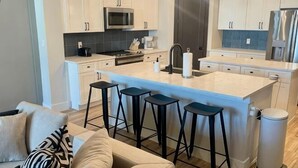 A modern kitchen with a central island, bar stools, and a trash can. - Loop, New Luxurious Large 3BR, Sleeps 9 + Parking (Collin County)