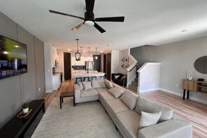 Een moderne woonkamer met een hoekbank, een plafondventilator, een flatscreen-tv en een eethoek op de achtergrond.