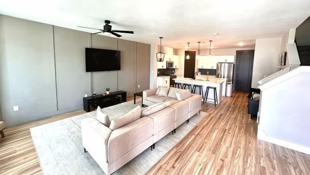 A modern living room with a sectional sofa, a flat-screen TV, and a ceiling fan. - Loop, New Luxurious Large 3BR, Sleeps 9 + Parking (Collin County)