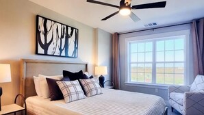 A hotel room with a bed, two bedside tables, a ceiling fan, a large window, and a view of the outdoors. - Loop, New Luxurious Large 3BR, Sleeps 9 + Parking (Collin County)