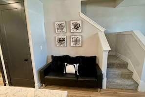 A living room with a dark-colored sofa, a white cushion, and four abstract wall art pieces. - Loop, New Luxurious Large 3BR, Sleeps 9 + Parking (Collin County)
