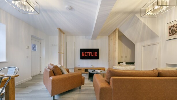 Moderni olohuone, jossa on nahkasohvat, sohvapöytä ja litteänäyttöinen televisio, jonka näytöllä näkyy teksti ’NETFLIX’.
