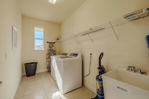 A laundry room with a washing machine, a vacuum cleaner, and a drying rack. - Villa Skye (Cape Coral)