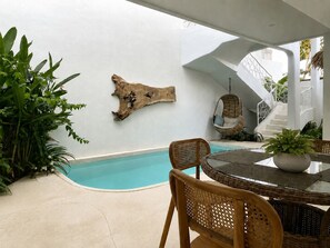 A poolside area with a hanging chair, a wooden wall art piece, and a dining table with chairs. - Villa Makuya (Ungasan)