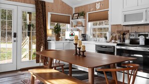 A kitchen with wooden cabinets, a dining table with benches, and a microwave. - Creekside Cabin W/ Pool Access & Private Hot Tub Near Thunder Ridge • Sleeps 4 (Blue Eye)