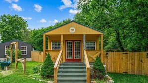 A small wooden building with a red door, a porch, and a staircase leading up to it. - Creekside Cabin W/ Pool Access & Private Hot Tub Near Thunder Ridge • Sleeps 4 (Blue Eye)
