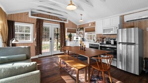 A modern kitchen with wooden walls, a stainless steel refrigerator, and a dining area with a wooden table and benches. - Creekside Cabin W/ Pool Access & Private Hot Tub Near Thunder Ridge • Sleeps 4 (Blue Eye)