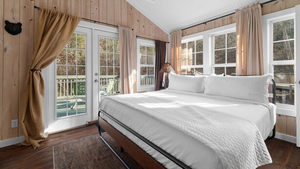 A bedroom with a large bed, wooden walls, and multiple windows. - Creekside Cabin W/ Pool Access & Private Hot Tub Near Thunder Ridge • Sleeps 4 (Blue Eye)