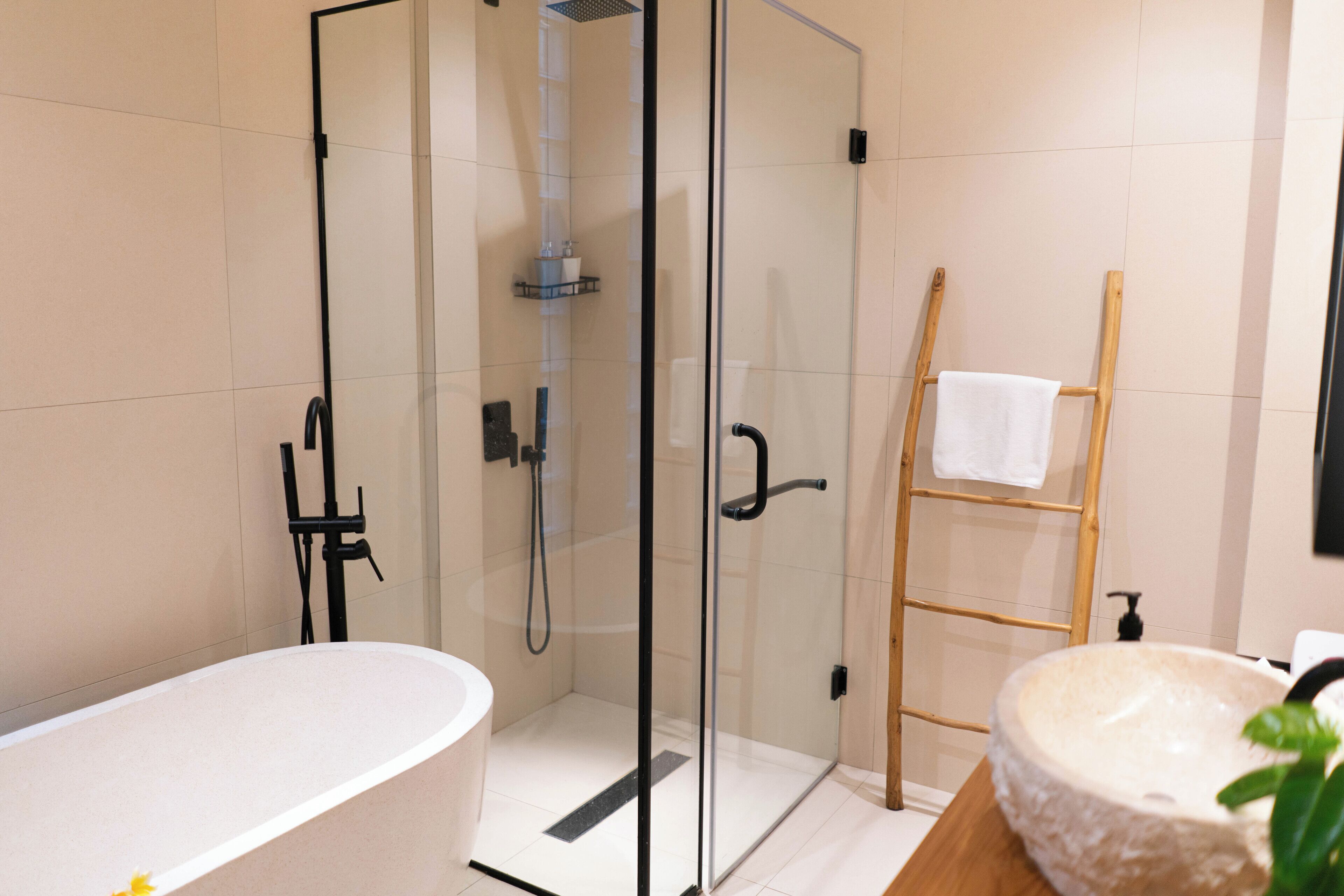 A modern bathroom with a glass-enclosed shower, a freestanding bathtub, and a wooden ladder with a towel.