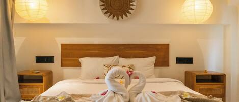 A hotel room with a bed, two bedside tables, a wooden headboard, and two hanging paper lanterns.