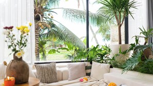 A cozy living room with a sofa, a small table with a candle, and a view of palm trees outside. - Dzen Greenfield Villa 7 (Pejeng)