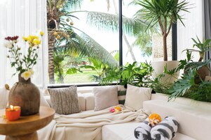 Una sala de estar acogedora con un sofá, una mesita con una vela y vistas a palmeras al exterior.