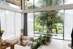 Una sala de estar moderna con un ventanal grande que da a un jardín tropical y una piscina.