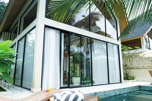 Una casa moderna con amplios ventanales, piscina y abundante vegetación.