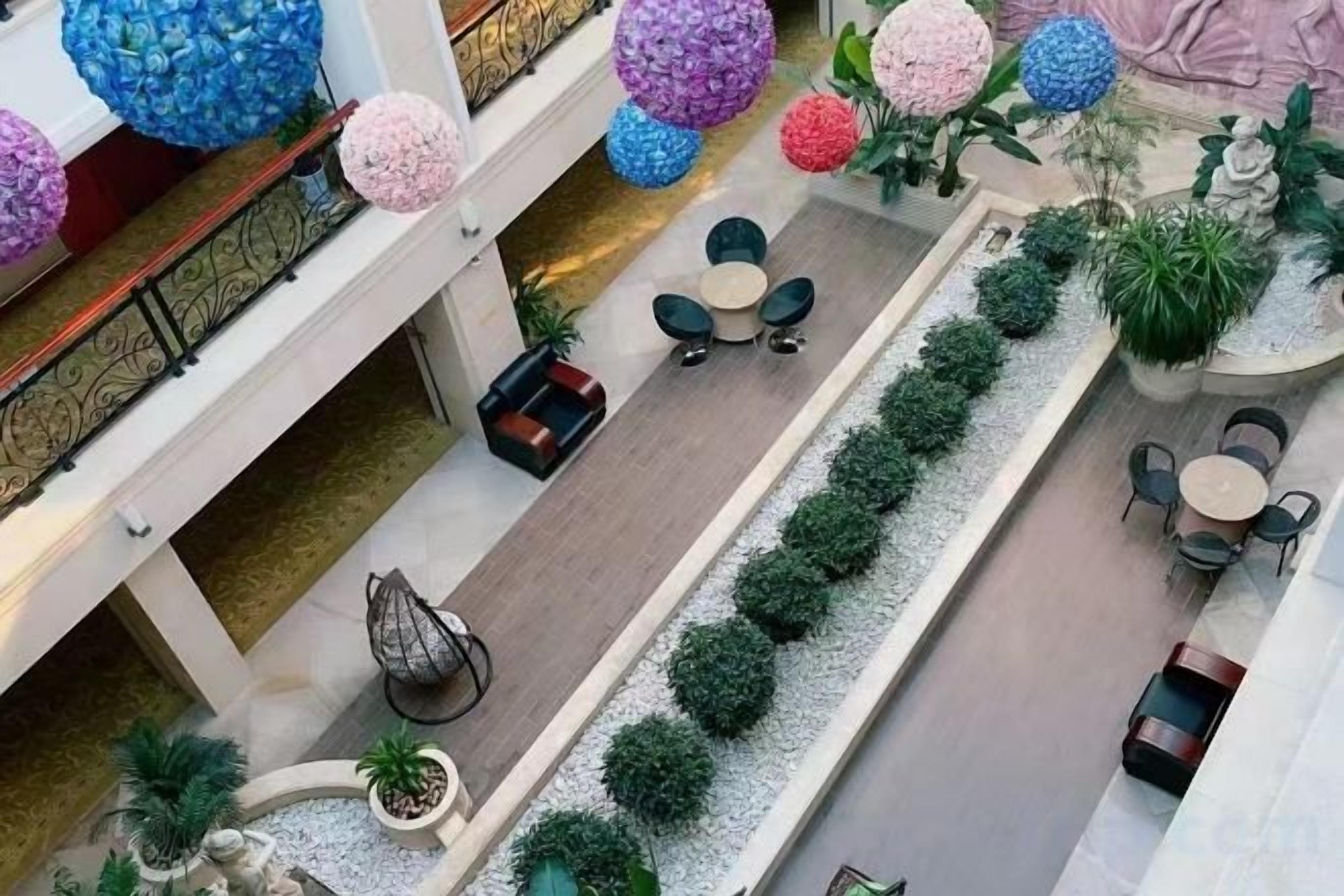 En atrium med flera våningsplan, utrustad med sittområden, en central plantering med grönska och dekorativa, sfäriska ornament.